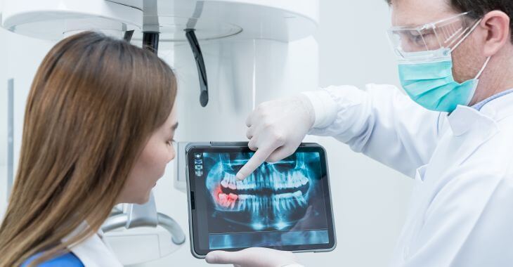 A dentist with patient's dental x-ray explaining wisdom tooth extraction procedure.