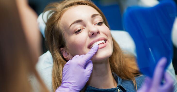 A dentist and a woman after permanent crown placing looking at her teeth in a mirror. 