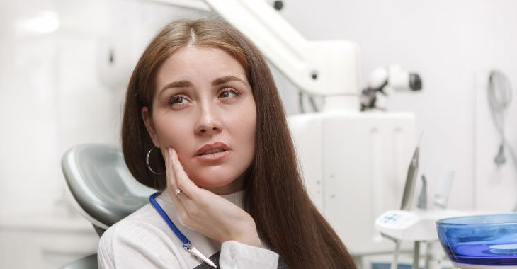 A concerned woman with dental issue sitting in a dental chair and pointing at her jaw.