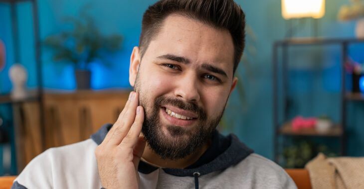 A man with dental issue causing discomfort touching his jaw