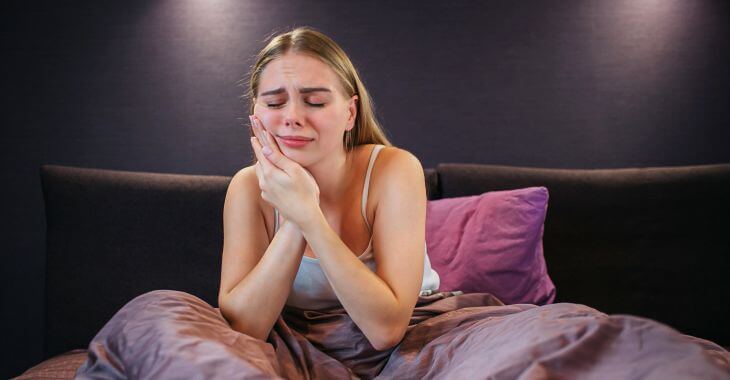 A woman with severe tooth pain unable to sleep sitting at night in her bed.