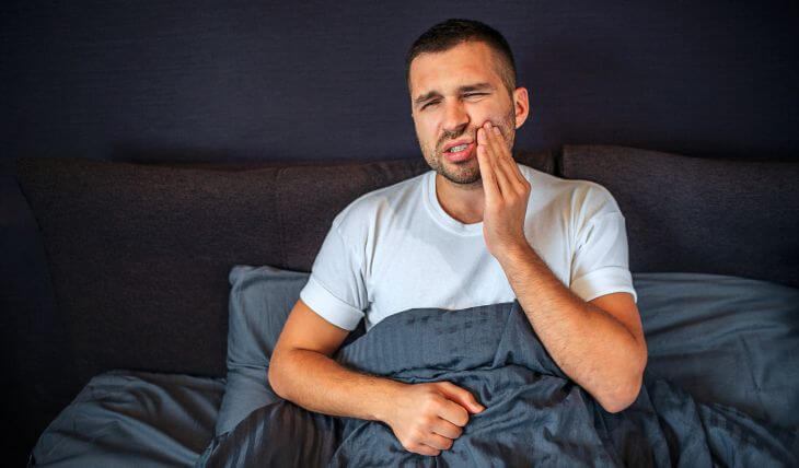 A man with severe tooth pain unable to sleep sitting at night in her bed.