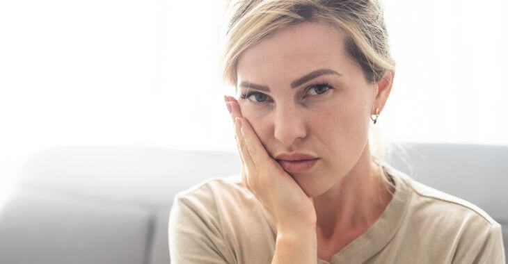 A woman with dental issue touching her cheek