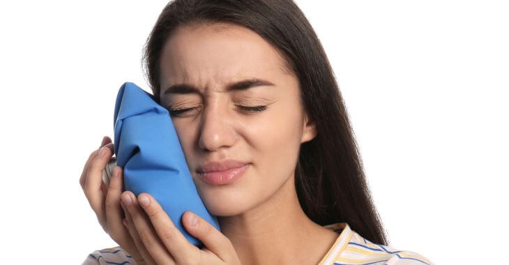 Young woman with pain caused by erupting wisdom tooth pressing a cold compress to her jaw.