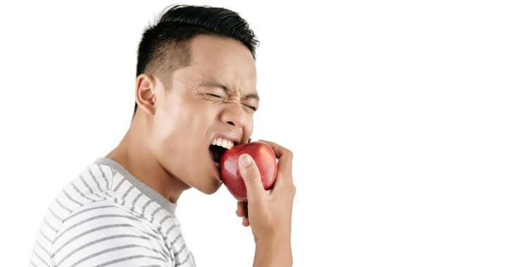 An Asian man feeling tooth pain when biting down an apple