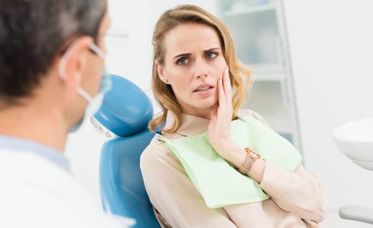 A concerned woman with dental issue sitting in a dental chair and talking to a dentist