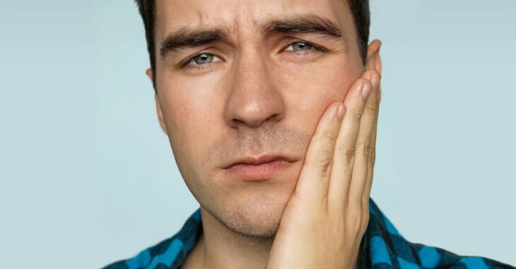 A concerned man with dental pain touching his cheek and jaw with his hand.