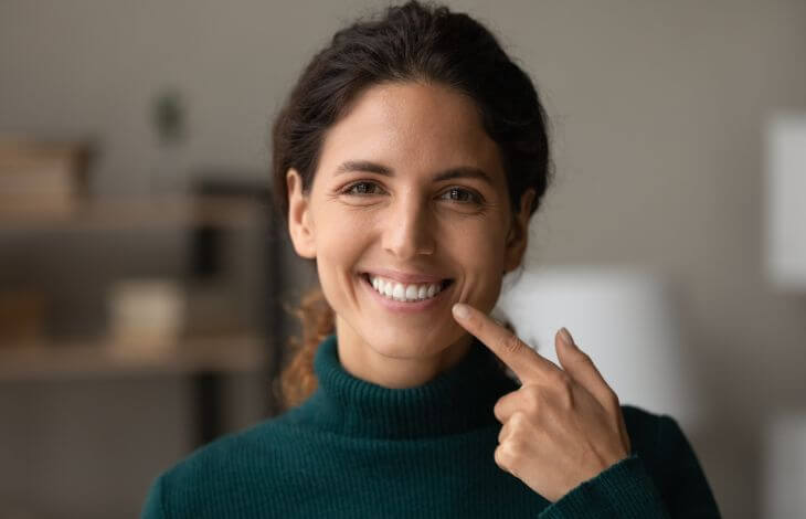 A happy woman with a perfect smile pointing at her teeth